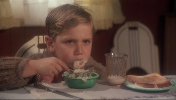 Movie still from “A Christmas Story” (1983), directed by Bob Clark – A young boy is eating a bowl of cereal; Medium shot, High angle