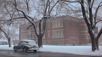 Movie still from “A Christmas Story” (1983), directed by Bob Clark – A car parked on the side of the road near a building; Extreme Wide shot, Low angle