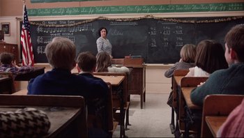 Movie still from “A Christmas Story” (1983), directed by Bob Clark – A woman standing in front of chalkboards in a class room; Wide shot, High angle