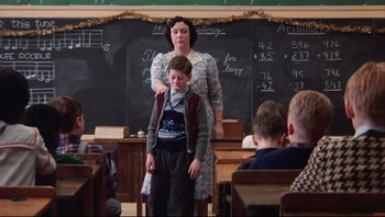 Movie still from “A Christmas Story” (1983), directed by Bob Clark – A woman standing next to a boy in front of a chalkboard; Medium shot, Over the shoulder angle