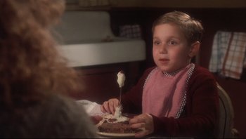 Movie still from “A Christmas Story” (1983), directed by Bob Clark – A young boy sitting at a table with a plate of food; Medium shot, High angle