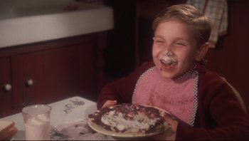Movie still from “A Christmas Story” (1983), directed by Bob Clark – A young boy is eating a cake on a plate; Close Up shot, High angle