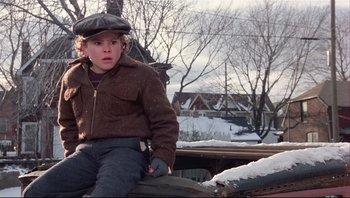 Movie still from “A Christmas Story” (1983), directed by Bob Clark – A young boy sitting on top of a tree trunk; Close Up shot, High angle