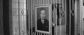 Movie still from “A Colt Is My Passport” (1967), directed by Takashi Nomura – An old photo of a man in a suit hanging on a wall; Medium shot, Low angle