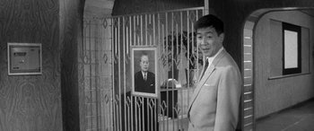 Movie still from “A Colt Is My Passport” (1967), directed by Takashi Nomura – A black and white photo of a man standing in front of a picture; Medium shot, Low angle