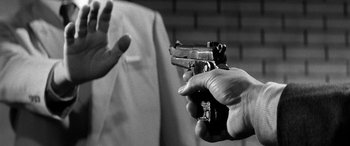Movie still from “A Colt Is My Passport” (1967), directed by Takashi Nomura – A man holding a gun pointed at another man; Extreme Close Up shot, Low angle
