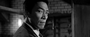 Movie still from “A Colt Is My Passport” (1967), directed by Takashi Nomura – Black and white photograph of a man wearing a suit and tie; Close Up shot, Low angle