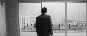 Movie still from “A Colt Is My Passport” (1967), directed by Takashi Nomura – A black and white photo of a man looking out of a window; Medium shot, Low angle