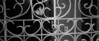 Movie still from “A Colt Is My Passport” (1967), directed by Takashi Nomura – A man is looking through a gate to see if he can find his cell phone; Extreme Close Up shot, High angle