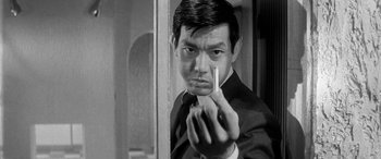 Movie still from “A Colt Is My Passport” (1967), directed by Takashi Nomura – A black and white photo of a man holding a cigarette; Close Up shot, Low angle