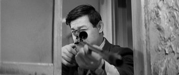 Movie still from “A Colt Is My Passport” (1967), directed by Takashi Nomura – A black and white photo of a man holding a rifle; Close Up shot, Low angle