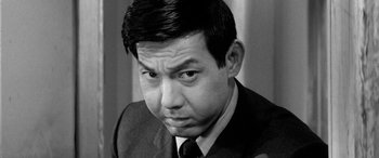 Movie still from “A Colt Is My Passport” (1967), directed by Takashi Nomura – Black and white photograph of a man in a suit and tie; Close Up shot, Low angle
