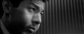 Movie still from “A Colt Is My Passport” (1967), directed by Takashi Nomura – A man's face in black - and - white; Extreme Close Up shot, Low angle