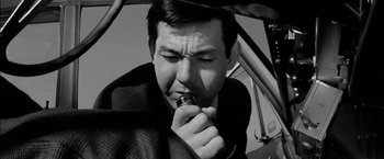Movie still from “A Colt Is My Passport” (1967), directed by Takashi Nomura – A black and white photo of a man holding an object in his mouth; Close Up shot, Low angle
