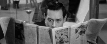 Movie still from “A Colt Is My Passport” (1967), directed by Takashi Nomura – A young man reading a newspaper in a cafe; Close Up shot, High angle