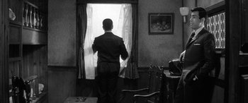 Movie still from “A Colt Is My Passport” (1967), directed by Takashi Nomura – A black and white photo of a man looking out of a window; Medium shot, High angle
