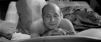 Movie still from “A Colt Is My Passport” (1967), directed by Takashi Nomura – An older man laying on his stomach with his eyes closed; Close Up shot, High angle