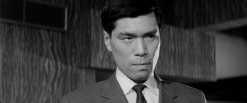 Movie still from “A Colt Is My Passport” (1967), directed by Takashi Nomura – Black and white photograph of a man wearing a suit and tie; Close Up shot, Low angle
