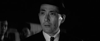 Movie still from “A Colt Is My Passport” (1967), directed by Takashi Nomura – A black and white photo of a man in a suit and hat; Close Up shot, Low angle