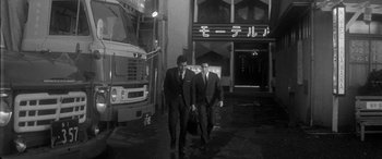 Movie still from “A Colt Is My Passport” (1967), directed by Takashi Nomura – A couple of men walking down a street; Wide shot, Low angle