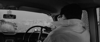 Movie still from “A Colt Is My Passport” (1967), directed by Takashi Nomura – A man sitting in the driver's seat of a car looking out the window; Medium shot, High angle