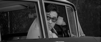 Movie still from “A Colt Is My Passport” (1967), directed by Takashi Nomura – A black and white photo of a man driving a car; Close Up shot, Over the shoulder angle
