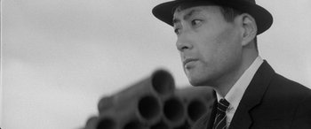 Movie still from “A Colt Is My Passport” (1967), directed by Takashi Nomura – A black and white photo of a man wearing a suit and hat; Close Up shot, Low angle