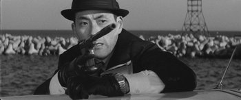 Movie still from “A Colt Is My Passport” (1967), directed by Takashi Nomura – A man in a hat holding a gun pointed at the camera; Close Up shot, Low angle