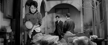 Movie still from “A Colt Is My Passport” (1967), directed by Takashi Nomura – A man and a woman standing next to each other in front of a building; Medium shot, Over the shoulder angle