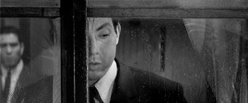 Movie still from “A Colt Is My Passport” (1967), directed by Takashi Nomura – A black and white photo of a man looking out a window; Close Up shot, Over the shoulder angle
