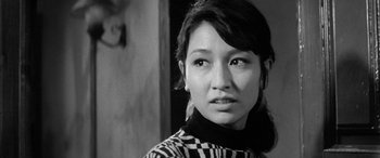 Movie still from “A Colt Is My Passport” (1967), directed by Takashi Nomura – A young woman in a checkered sweater looks at the camera; Close Up shot, Low angle