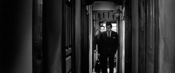 Movie still from “A Colt Is My Passport” (1967), directed by Takashi Nomura – A man in a suit and tie walking down a hall way; Medium shot, Low angle