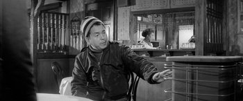 Movie still from “A Colt Is My Passport” (1967), directed by Takashi Nomura – A man sitting at a table in front of a mirror; Medium shot, Over the shoulder angle