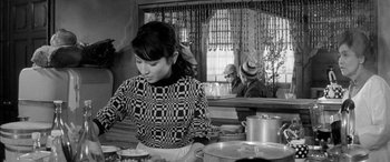 Movie still from “A Colt Is My Passport” (1967), directed by Takashi Nomura – A black and white photo of a woman sitting at a table; Medium shot, Over the shoulder angle