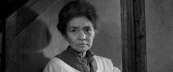 Movie still from “A Colt Is My Passport” (1967), directed by Takashi Nomura – An older woman wearing a white shirt and a neck tie; Close Up shot, Low angle