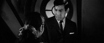 Movie still from “A Colt Is My Passport” (1967), directed by Takashi Nomura – A man in a suit and tie talking to a woman in a suit; Close Up shot, Over the shoulder angle