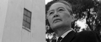 Movie still from “A Colt Is My Passport” (1967), directed by Takashi Nomura – An older man in a suit and tie looking upward; Close Up shot, Low angle