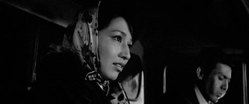 Movie still from “A Colt Is My Passport” (1967), directed by Takashi Nomura – A young woman wearing a headscarf in a car; Close Up shot, Low angle