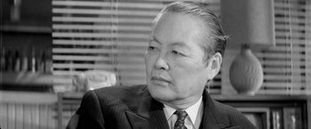 Movie still from “A Colt Is My Passport” (1967), directed by Takashi Nomura – An older man wearing a suit and tie; Close Up shot, Low angle