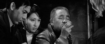 Movie still from “A Colt Is My Passport” (1967), directed by Takashi Nomura – A man and a woman sitting next to each other; Close Up shot, Low angle