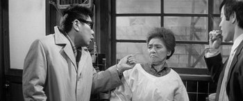 Movie still from “A Colt Is My Passport” (1967), directed by Takashi Nomura – An older woman and a younger man are pointing at each other; Medium shot, Over the shoulder angle