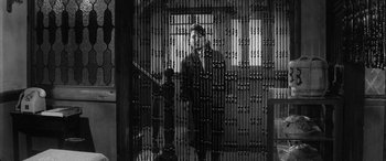 Movie still from “A Colt Is My Passport” (1967), directed by Takashi Nomura – A man standing in front of a metal fence; Medium shot, High angle