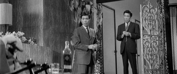 Movie still from “A Colt Is My Passport” (1967), directed by Takashi Nomura – A man in a suit standing next to another man in a suit; Medium shot, Low angle