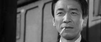 Movie still from “A Colt Is My Passport” (1967), directed by Takashi Nomura – Black and white photograph of a man smoking a cigarette; Close Up shot, Low angle