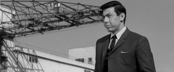 Movie still from “A Colt Is My Passport” (1967), directed by Takashi Nomura – Black and white photograph of a man wearing a suit and tie; Medium shot, Low angle