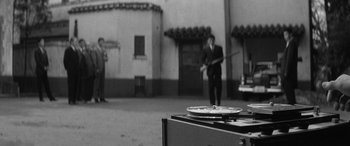Movie still from “A Colt Is My Passport” (1967), directed by Takashi Nomura – A man in a suit and tie holding a pole; Wide shot, High angle