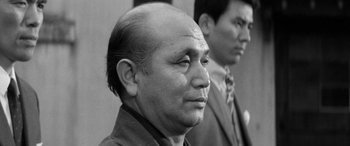 Movie still from “A Colt Is My Passport” (1967), directed by Takashi Nomura – A black - and - white photo of a man with a bald head; Close Up shot, Low angle