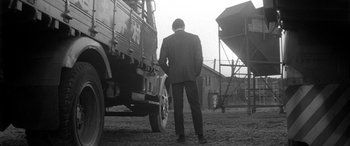 Movie still from “A Colt Is My Passport” (1967), directed by Takashi Nomura – A black and white photo of a man standing next to a truck; Wide shot, Low angle