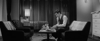 Movie still from “A Colt Is My Passport” (1967), directed by Takashi Nomura – A black and white photo of a man sitting at a coffee table; Medium shot, High angle