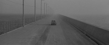 Movie still from “A Colt Is My Passport” (1967), directed by Takashi Nomura – A car driving down a road in the middle of the day; Extreme Wide shot, High angle